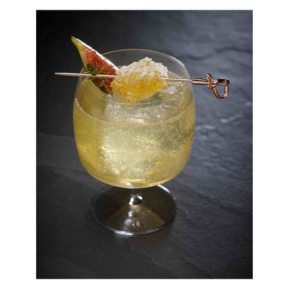 A sparkling, pale yellow cocktail in a wide-bowled stemmed glass, garnished with a slice of fig and a piece of honeycomb. The garnish is skewered on a copper-plated cocktail pick with a 4.5 inch Copper Plated Barfly Cocktail Pick, with a bamboo knot top.