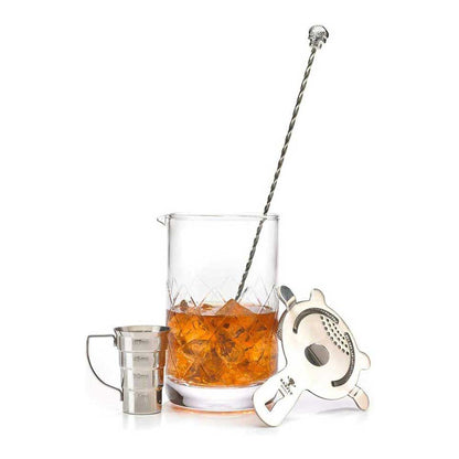 A Barfly Drink Mixing Glass, 24oz, 700ml with diamond pattern on a white background with cocktail ingredients, a strainer, a jigger, and a silver stirrer on a white background