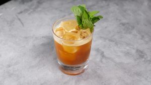 A cocktail in a rocks glass with ice cubes, garnished with fresh mint leaves.