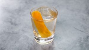 A cocktail with garnish and ice inside a chilled glass above a marble top table.