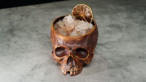 A skull-shaped glass filled with crushed ice and a lime wedge garnish.